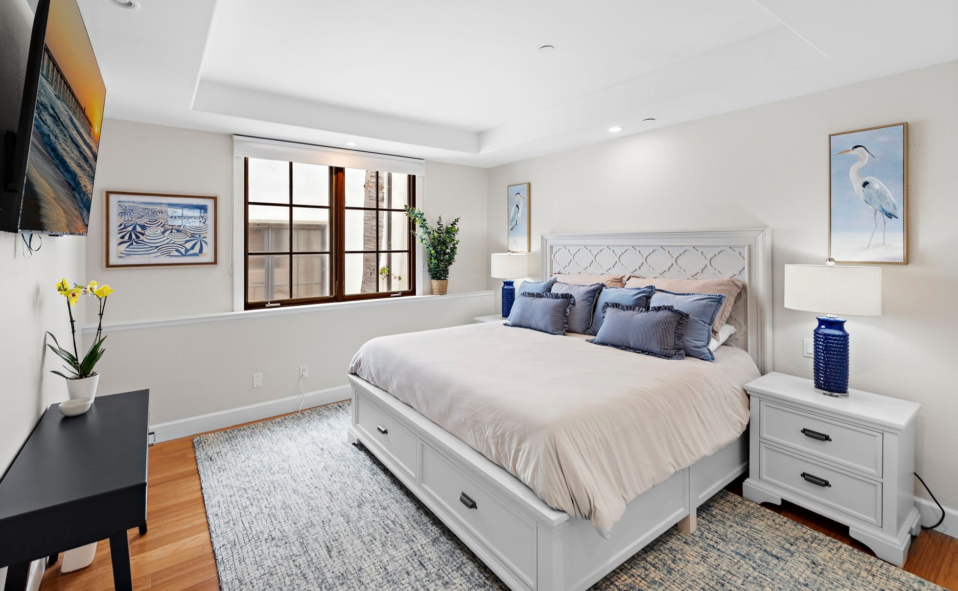 Enjoy a cozy primary bedroom with a plush king bed with premium linens, calming coastal décor, abundant natural light, and a large smart TV for winding down after a day at the beach