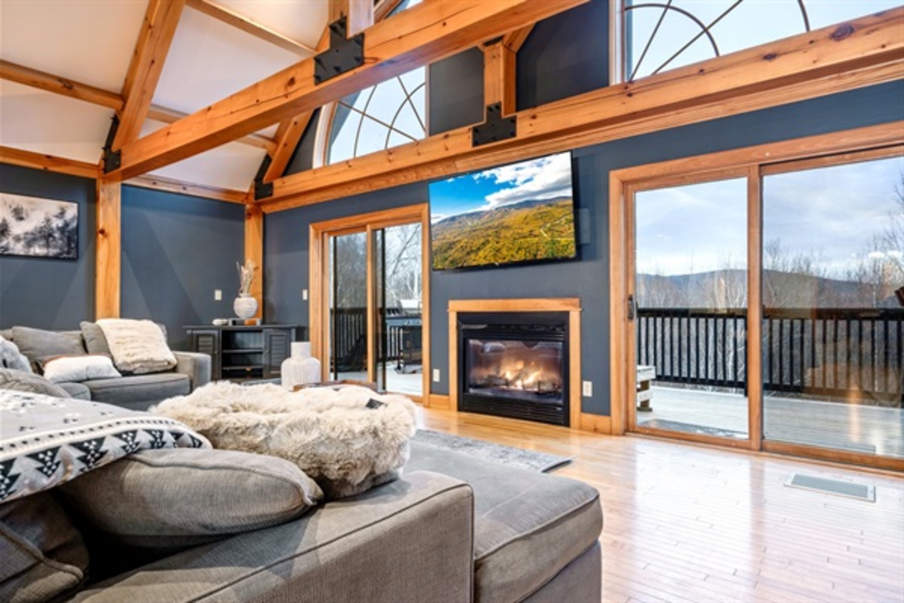 Relax beneath soaring timber beams as natural light, a cozy fireplace, and wall to wall windows create a stunning lodge style living space.