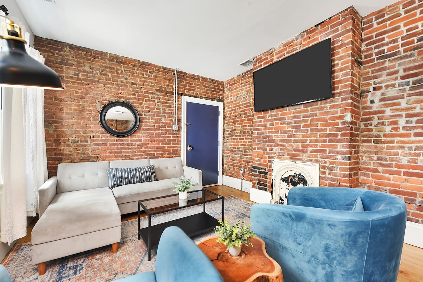 Relax in style on the L-shaped sofa, surrounded by a chic brick wall, floor-to-ceiling windows, and warm lighting. The perfect spot to unwind!