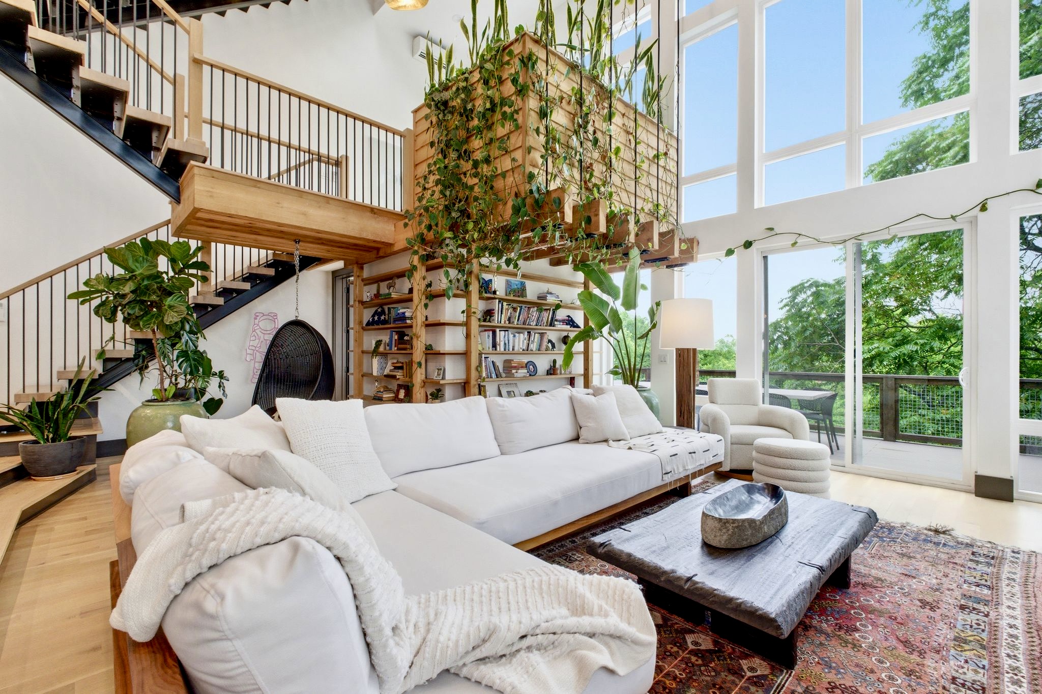 Breezy upper-level lounge w/ white sectional, trailing plants & treetop light pouring in.
