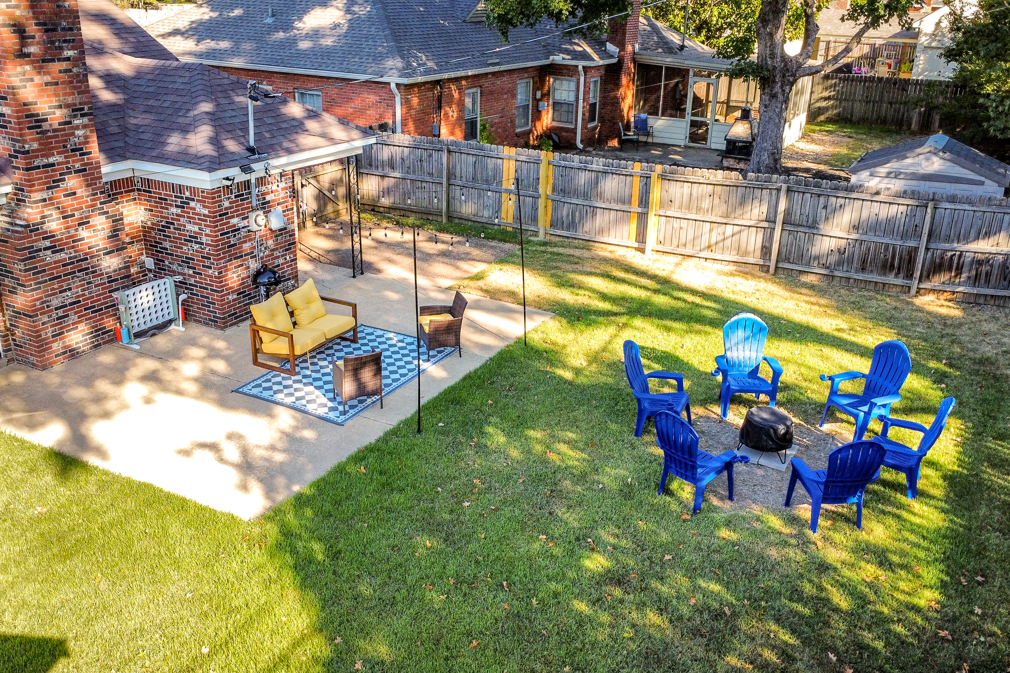 Fenced backyard with string-lit patio, fire pit, and electric grill.