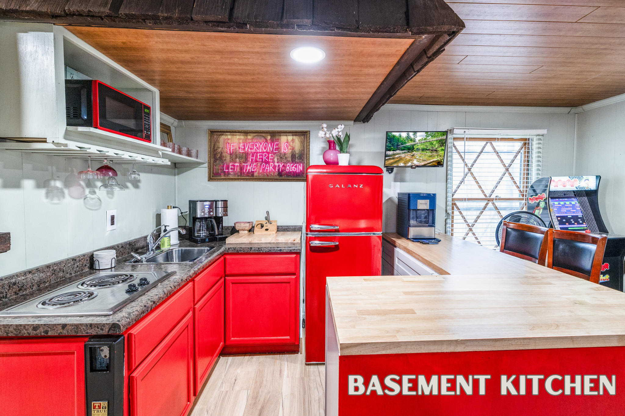 This vibrant retro kitchen features a red fridge, microwave, stovetop, coffee maker, and arcade games. The perfect spot for meals and snacks.