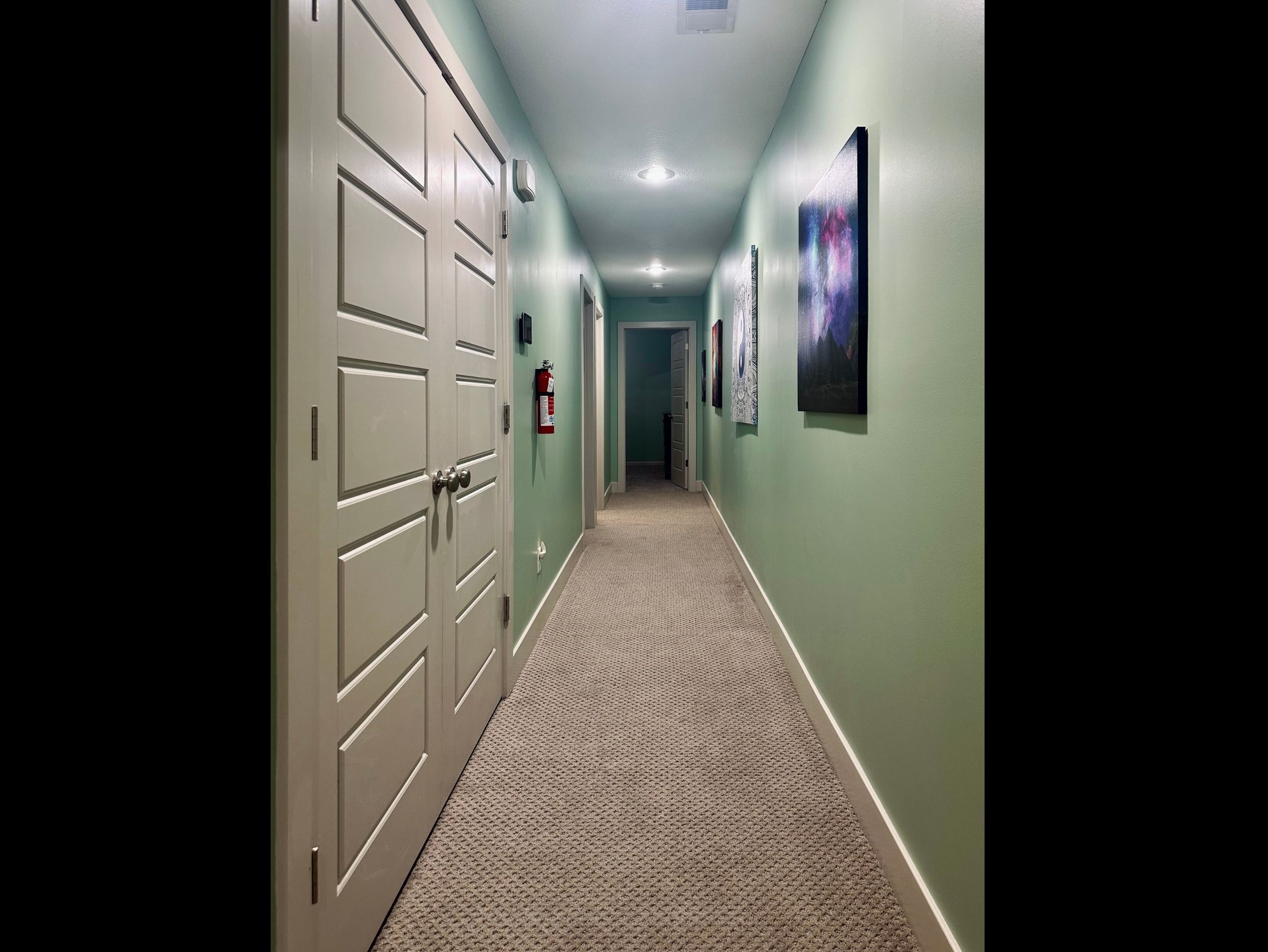 Upper-level hallway facing east toward Bedrooms 2 and 3, with double doors on the left concealing the conveniently located laundry area.