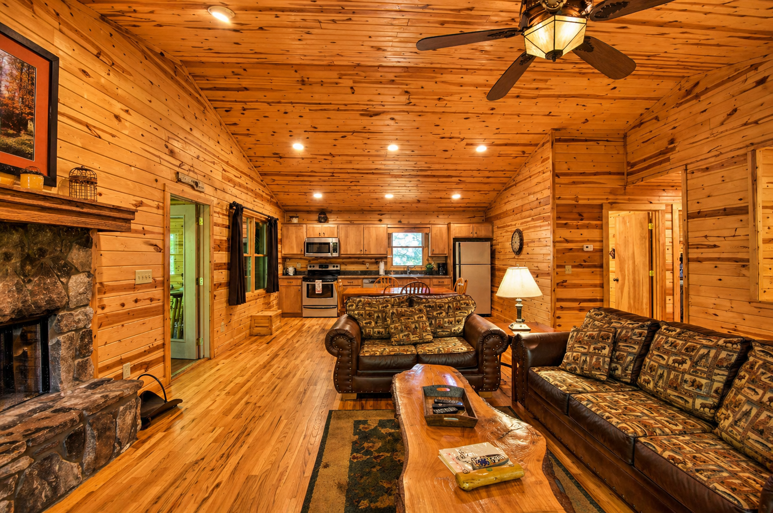 Spacious open-concept living with a cozy stone fireplace, vaulted wood ceilings, and a fully equipped kitchen—perfect for gathering and relaxing.