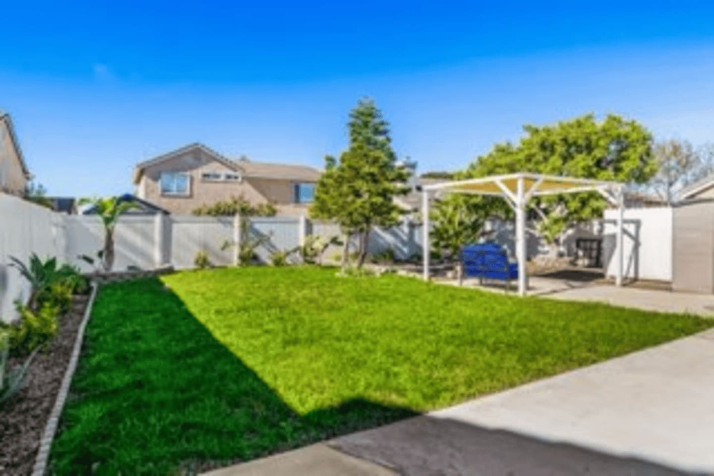 Spacious fenced backyard with shaded pergola seating and outdoor furniture, perfect for relaxing, enjoying the sunshine, or gathering with friends.