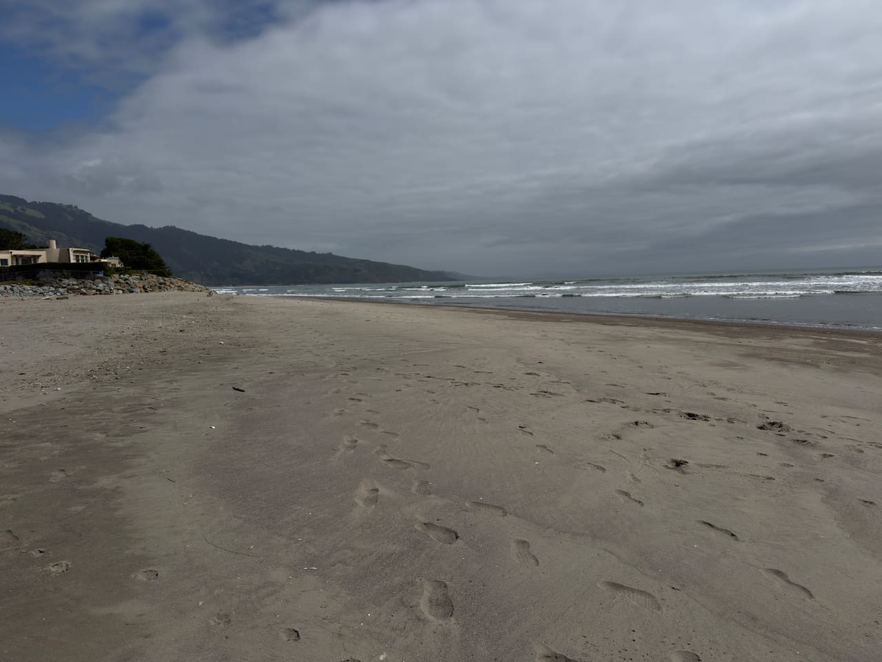 Wide sandy beach with waves and mountain views.

