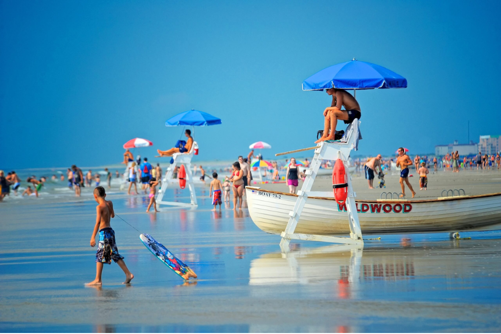 Lively beach scene with lifeguards on duty, wide sandy shoreline, and shallow waves along the coast. A classic beach day setting ideal for swimming, walking the shore, and enjoying the active seaside atmosphere nearby.