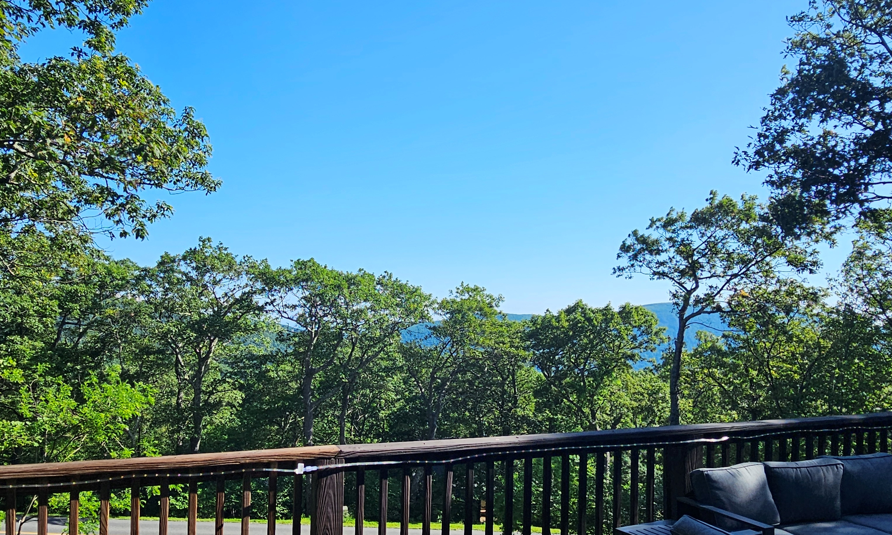 Framed in lush summer greens, the distant ridge-lines create a stunning backdrop for refreshments, conversation, or simply listening to the trees rustle