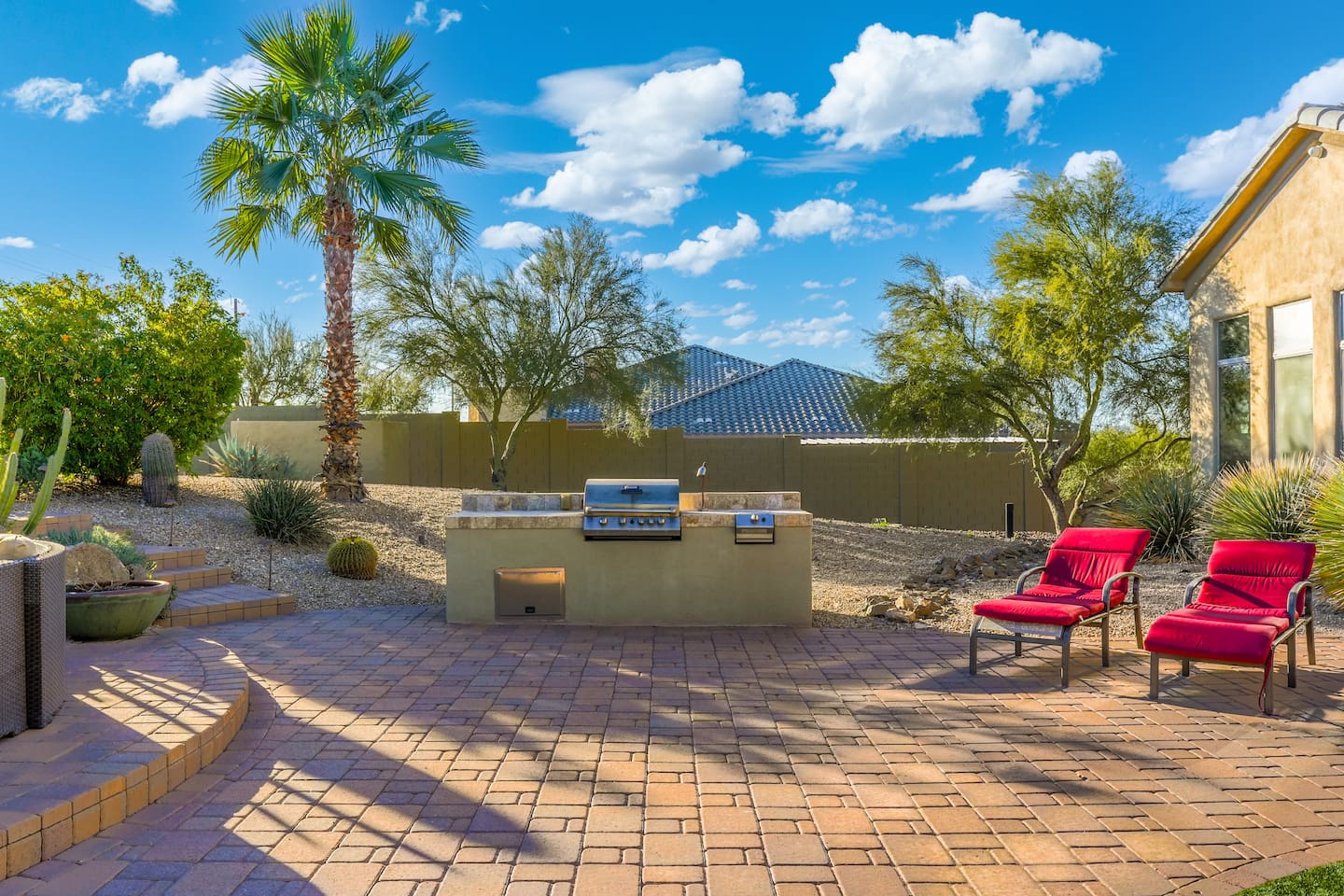 Sun-soaked patio with built-in BBQ and red loungers—perfect for outdoor cooking and relaxing.