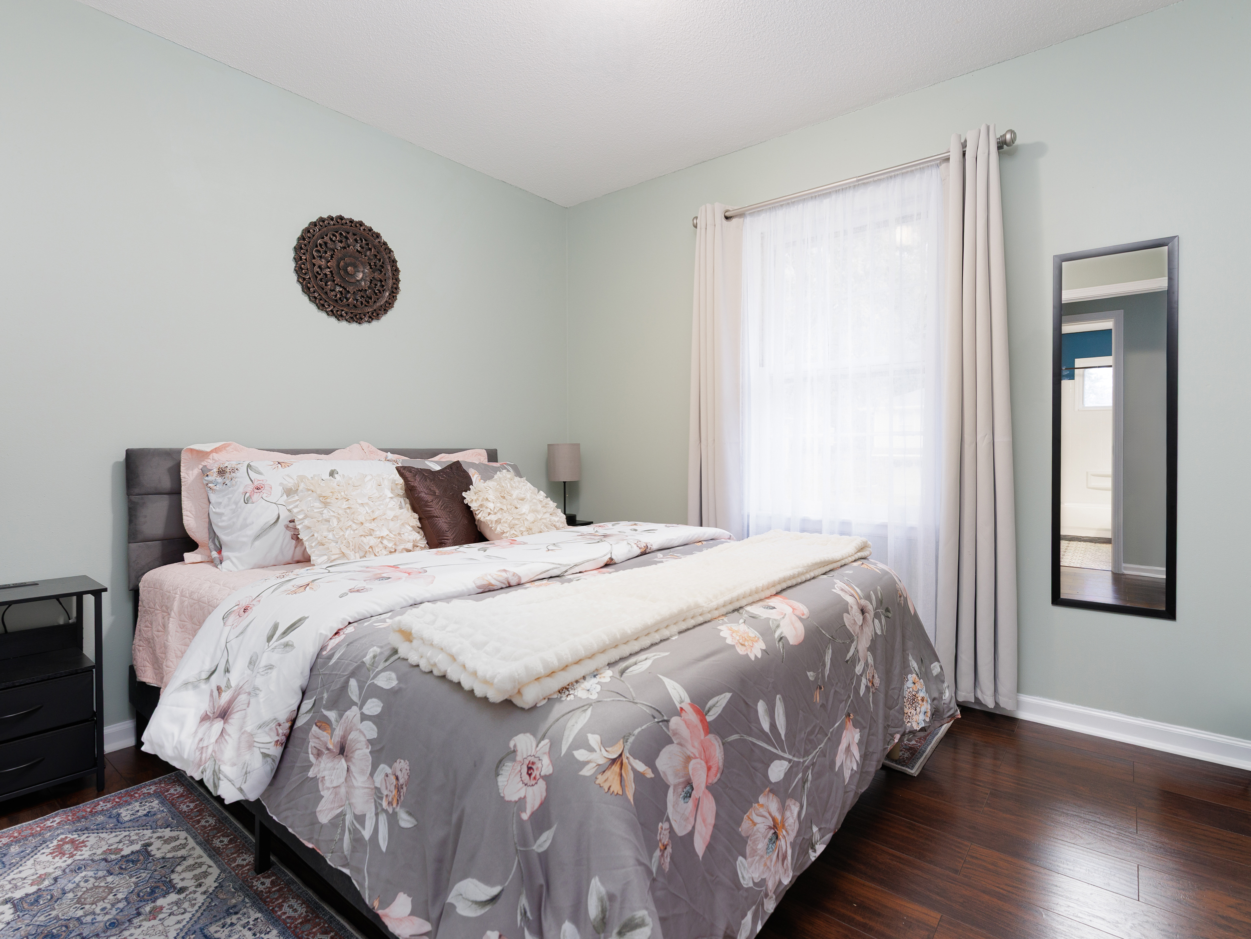 Additional guest bedroom with queen bed, hardwood floors, and a bright, airy feel.