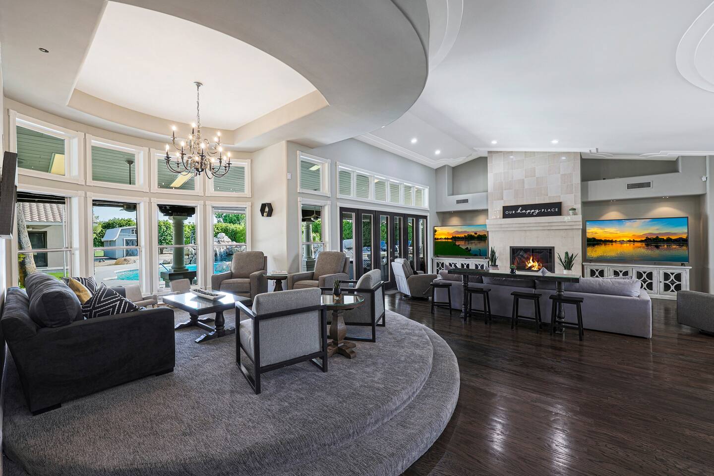 Gather in style in this expansive living space featuring a sophisticated sunken lounge, cozy fireplace, and walls of windows bringing in natural light and poolside views.