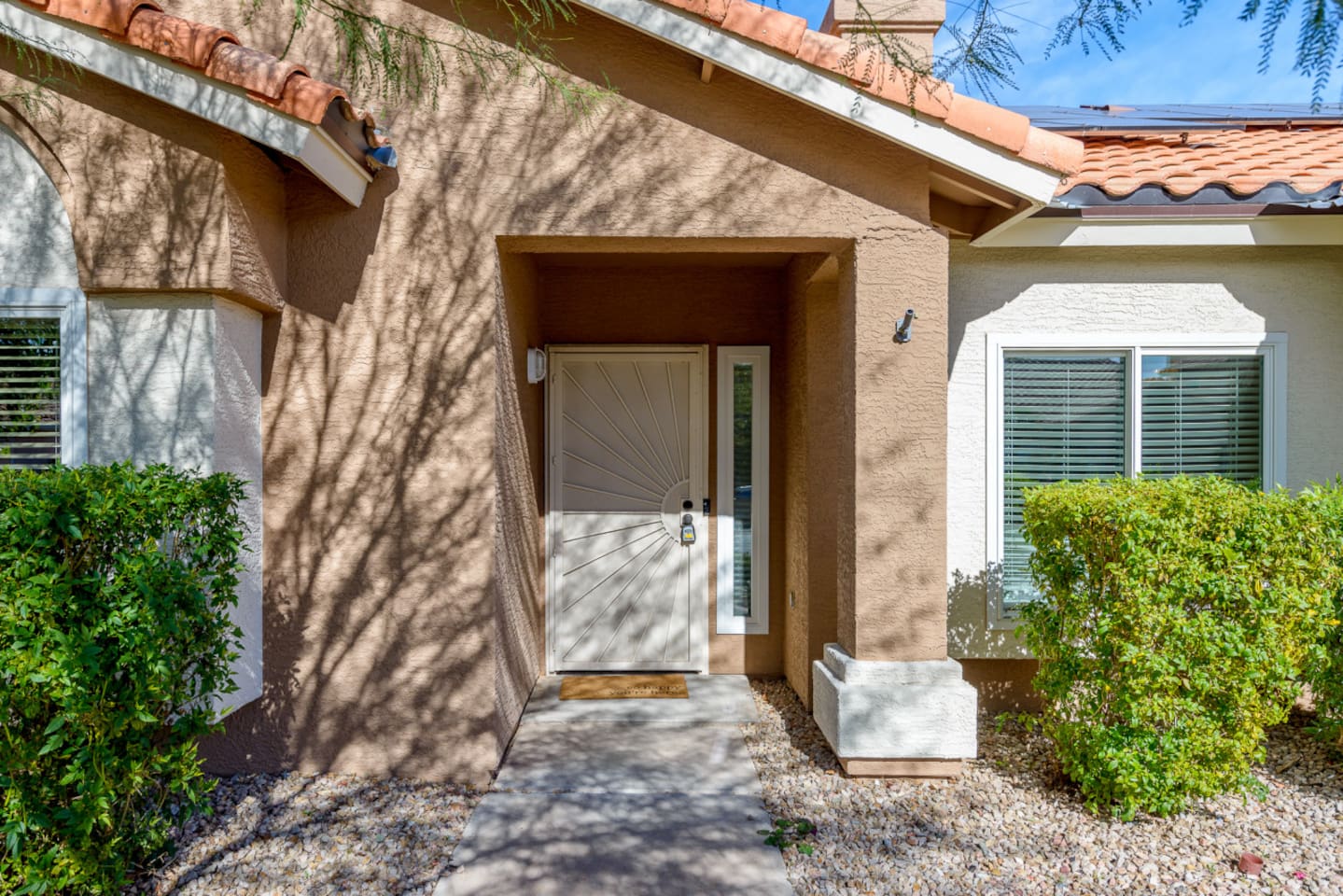 Front entry with covered walkway, desert landscaping, and a simple arrival path to the home.