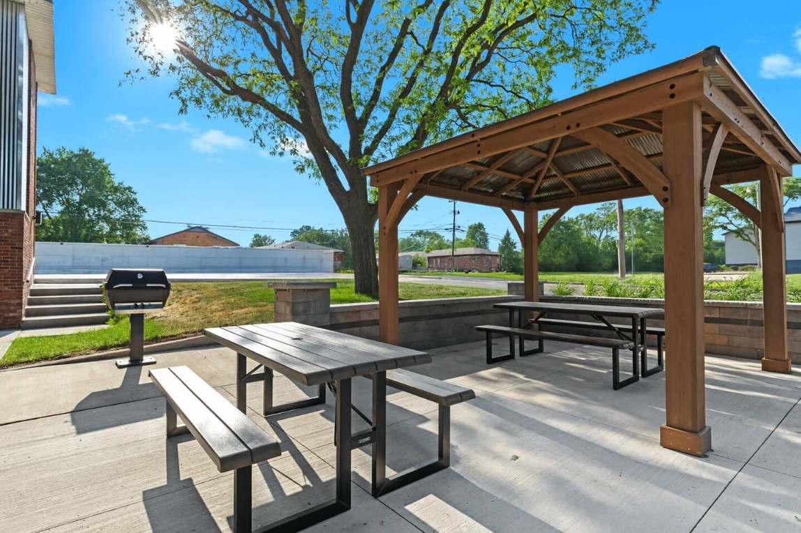 Dine al fresco under the shade of a modern pergola, complete with picnic tables and nearby grill access.