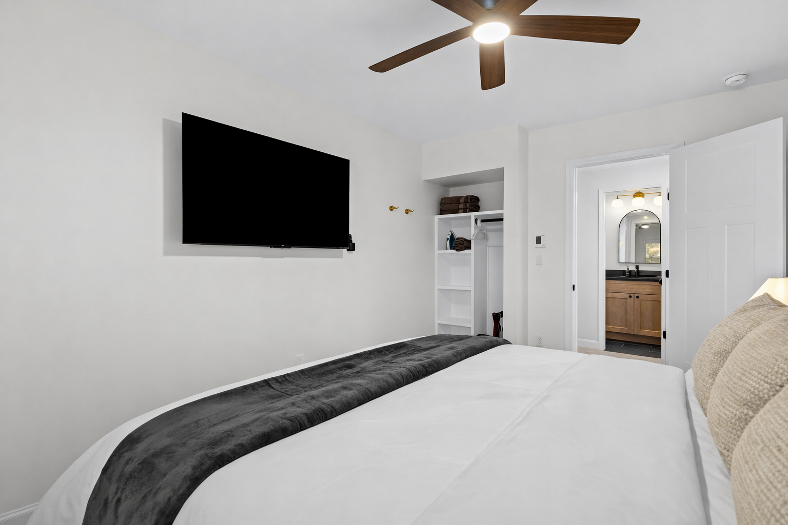 Unwind in this spacious bedroom featuring a plush bed, smart TV, ceiling fan, and easy access to the bathroom for a comfortable, restful stay.