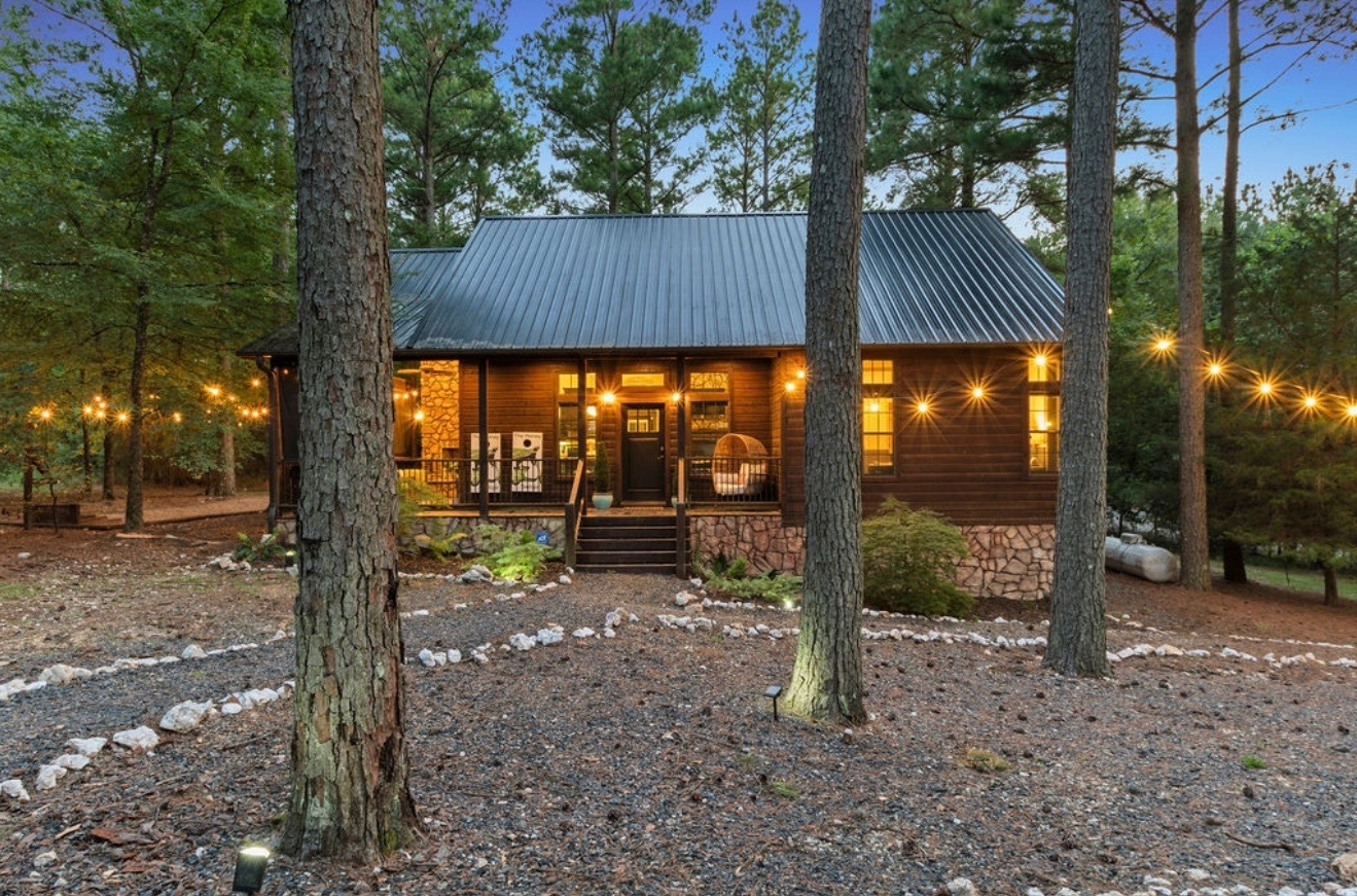 The cabin exterior transforms at dusk with sparkling lights and forest views, creating a cozy, romantic retreat.