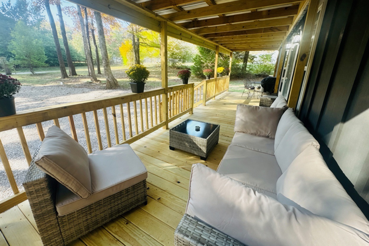 Large covered porch with sectional sofa, coffee table, dining set & grill — perfect for relaxing in the woods