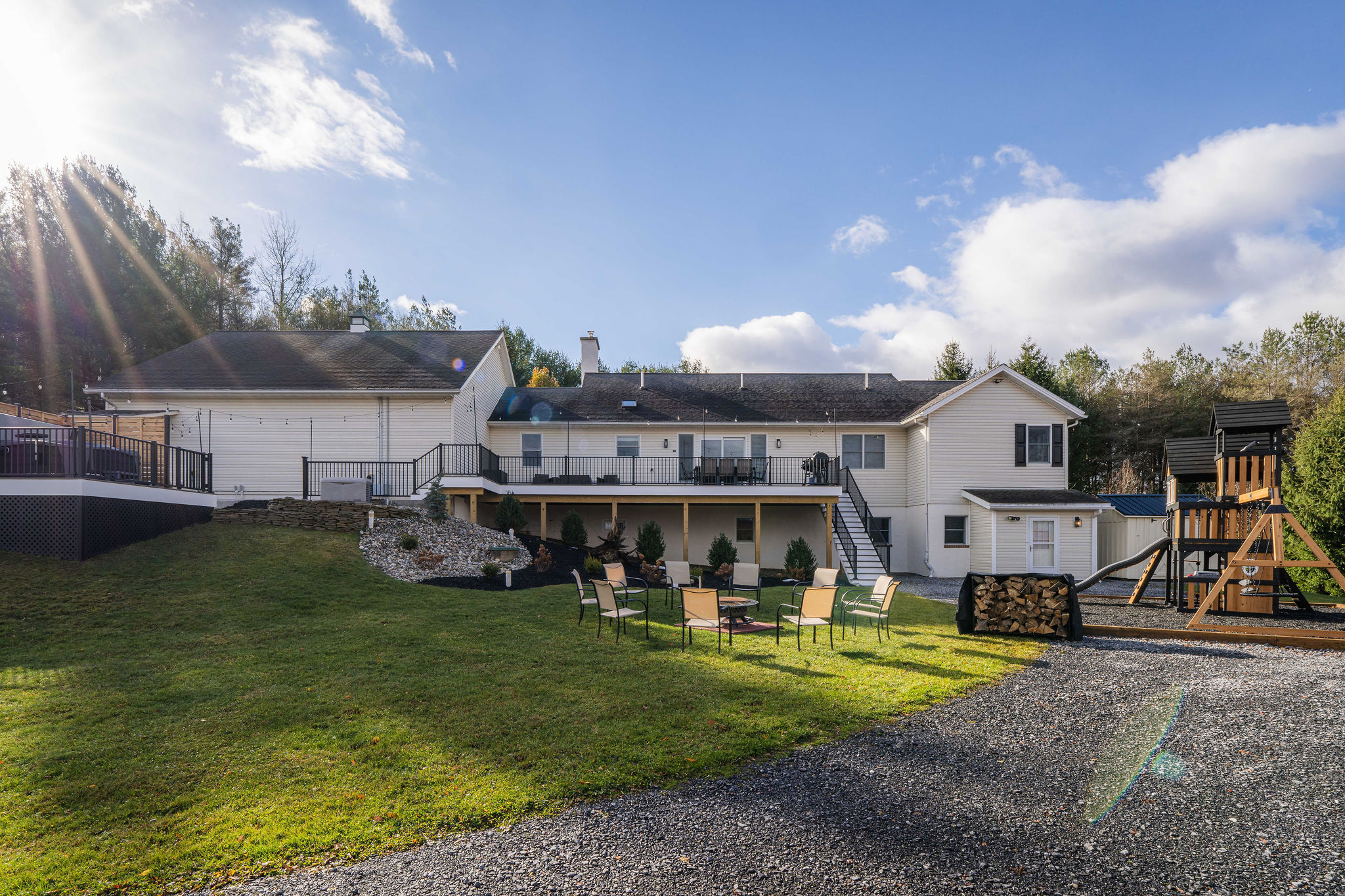 Sunny daytime view of the large backyard with fire pit and kids’ playset