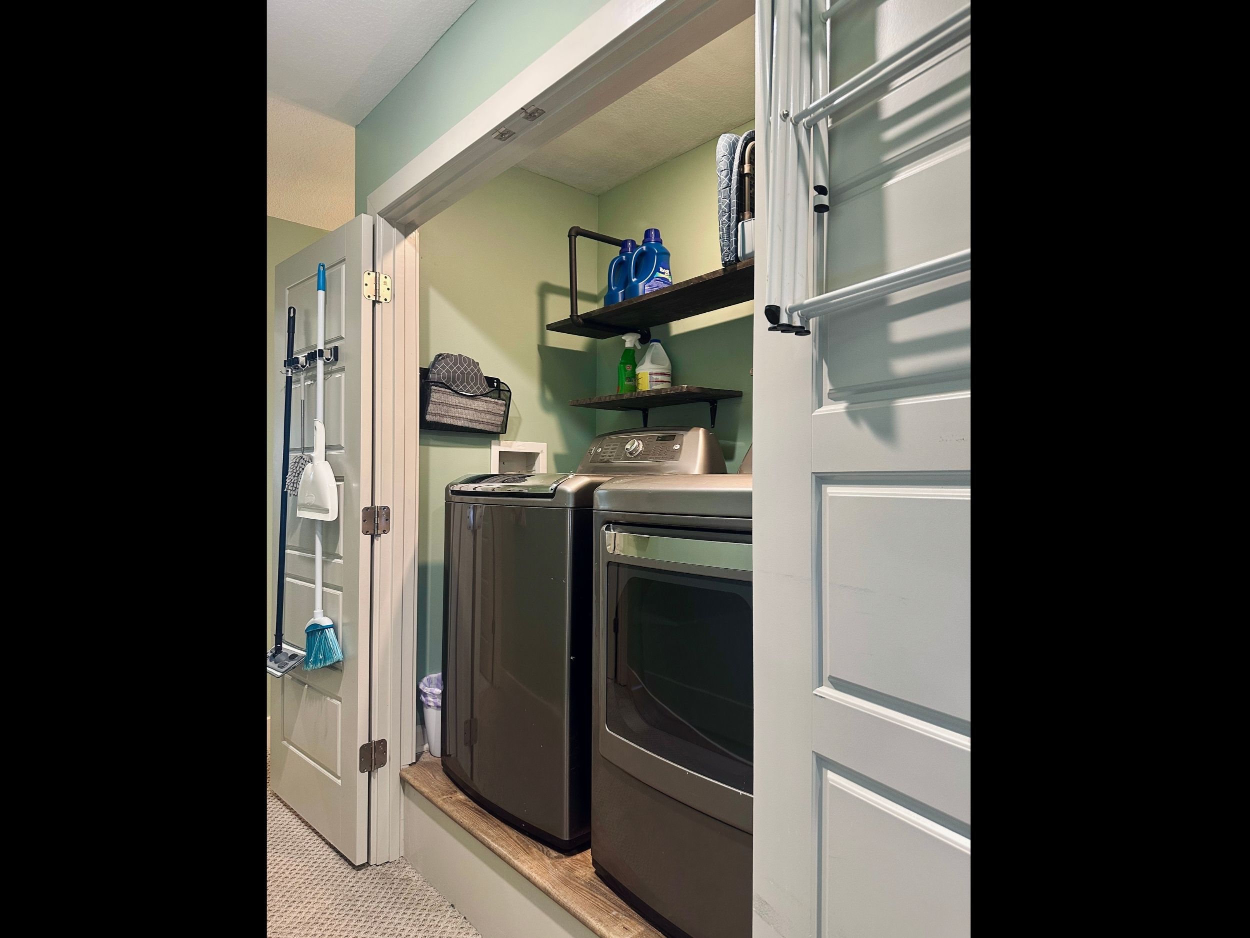 Fully equipped laundry area with detergent, bleach, stain remover, and mounted cleaning tools including mop, broom, duster, and extra mop pads.
