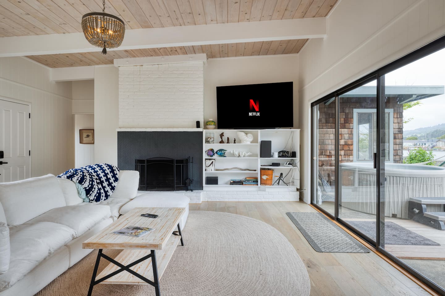 - Comfortable living area with fireplace, TV, and built in shelving decor  
- Sliding glass doors open directly to the patio and hot tub area outside  
- Soft neutral tones create a calming, welcoming atmosphere for guests  
