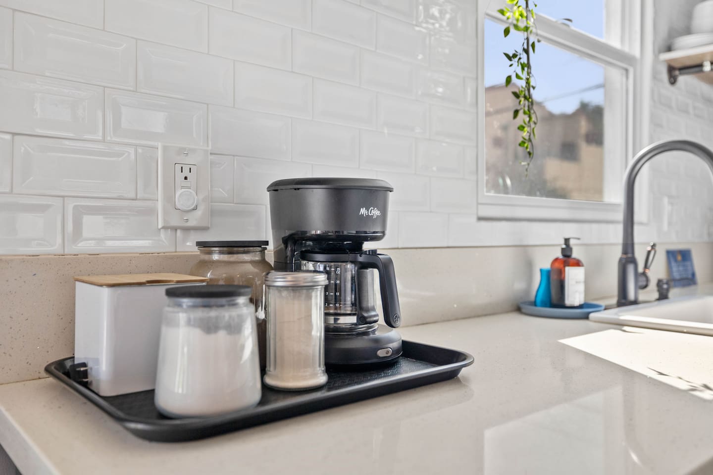 A sleek coffee maker accompanied by coffee mate, sugar, and stylish mugs. The arrangement invites guests to brew their perfect cup, creating a cozy atmosphere for enjoying morning rituals or afternoon breaks in this well-equipped space.