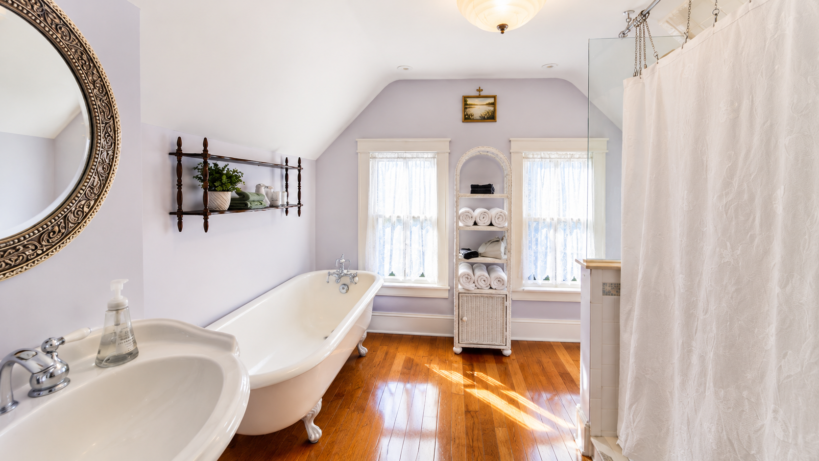 The third floor full bath — a clawfoot tub, original hardwood floors, and lavender walls under a vaulted ceiling. This one might be hard to leave.
