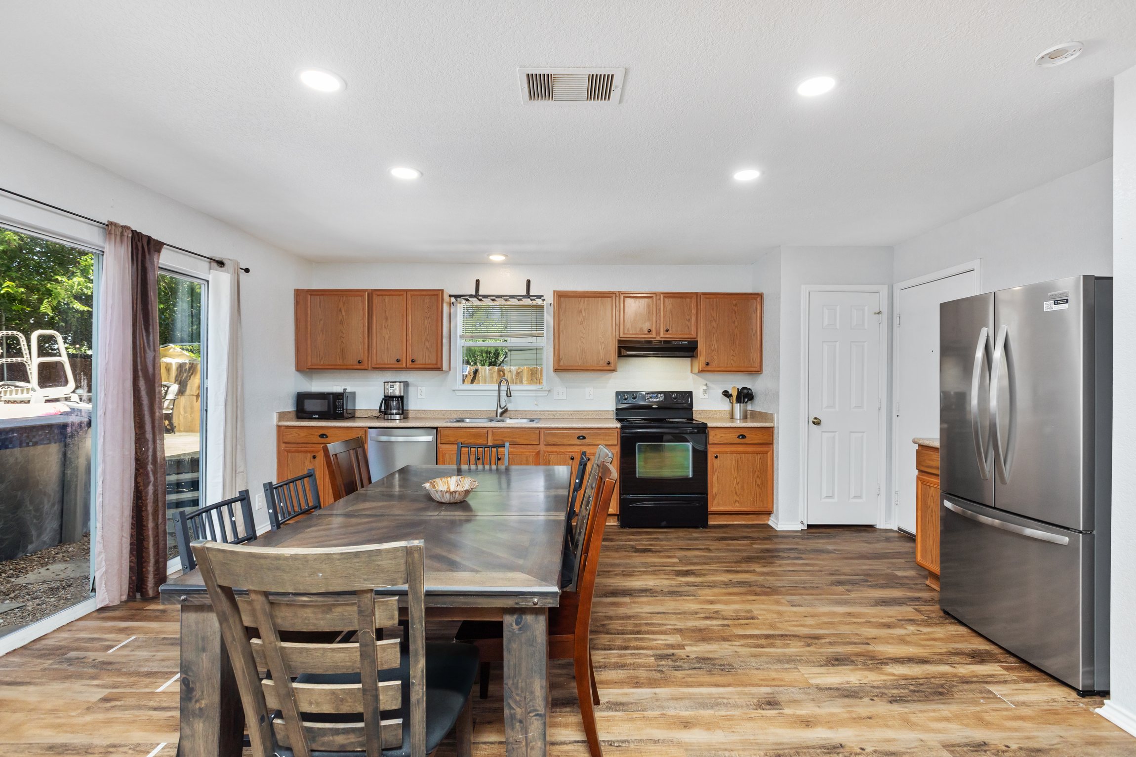 Bright kitchen and dining space with stainless refrigerator, full appliances, and group dining table. Natural light and open layout — perfect for families settling in for a week-long stay near Randolph AFB.