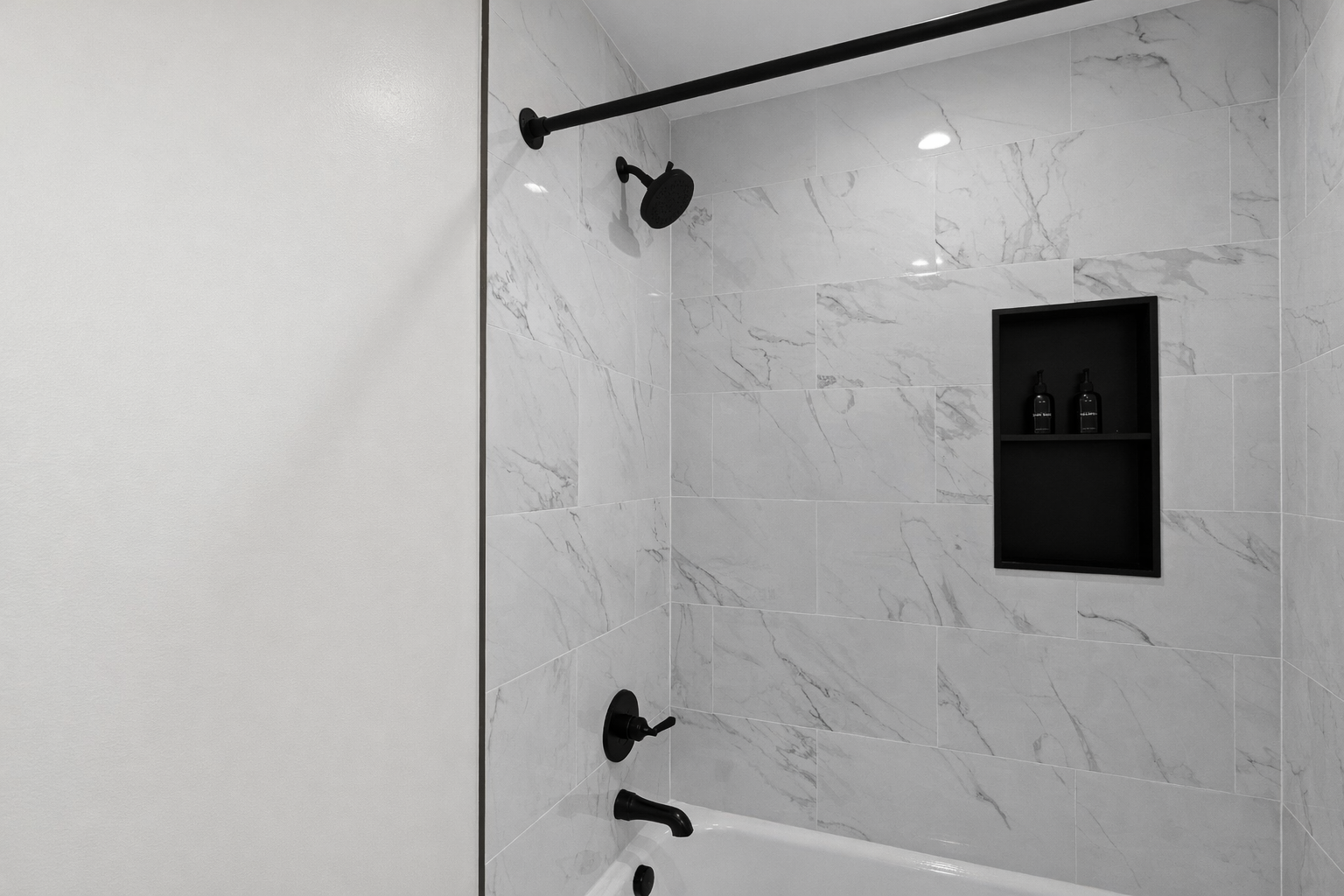 Sleek tub-shower with marble-style tile, matte black fixtures, and built-in shelving—clean, modern, and perfect for a refreshing start or relaxing soak.