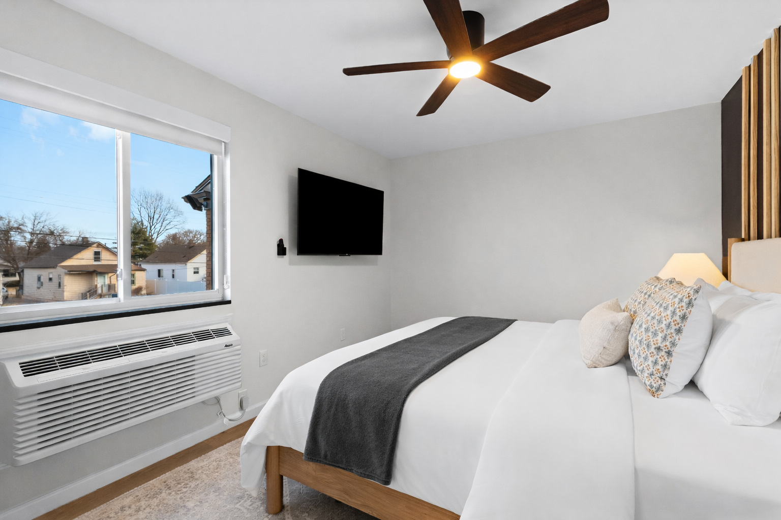 Bright, calming bedroom with plush bed, ceiling fan, and wall-mounted TV—designed for comfort, relaxation, and restful nights.