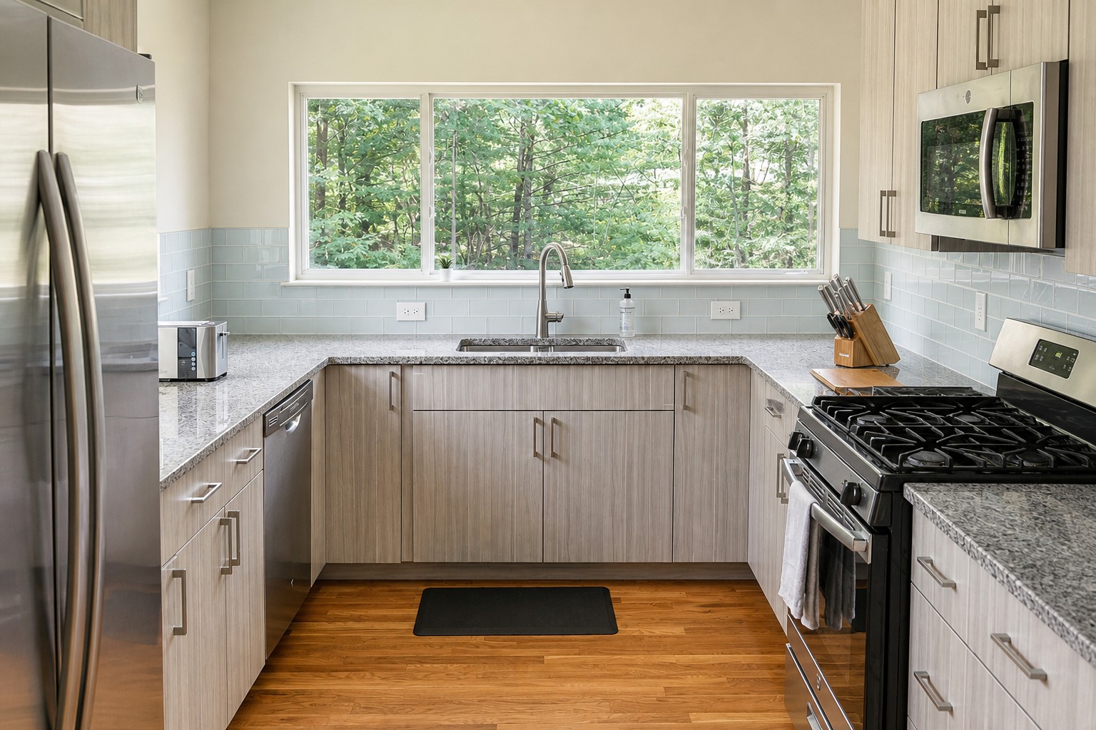 Full kitchen with granite counters, a gas range and a wall of windows onto the woods