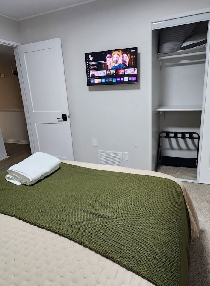 This bright queen bedroom offers a cozy retreat with a Smart TV with streaming services, blackout curtains, and a quiet ceiling fan for uninterrupted sleep. The queen bed is dressed with premium linens and supportive pillows.