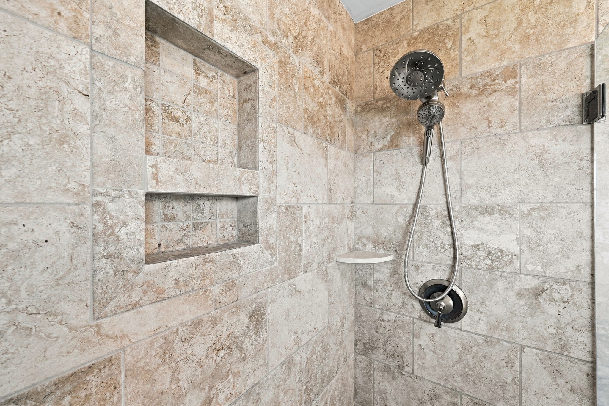Beautifully tiled walk-in shower featuring modern fixtures and built-in storage niches