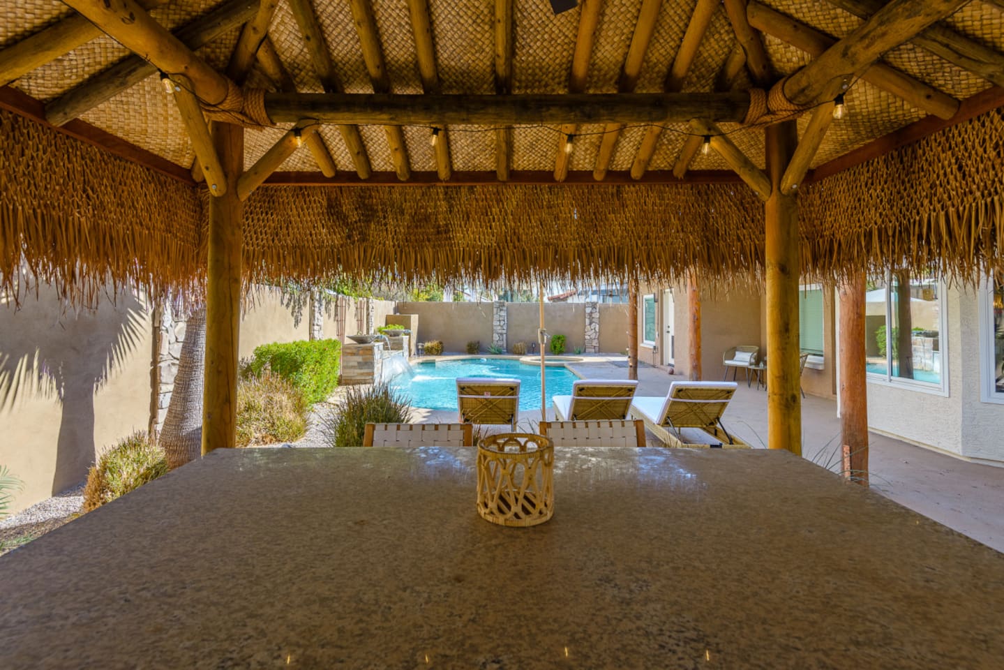 Covered patio dining area with BBQ grill, pool views, and easy access to the tiki lounge and backyard seating.