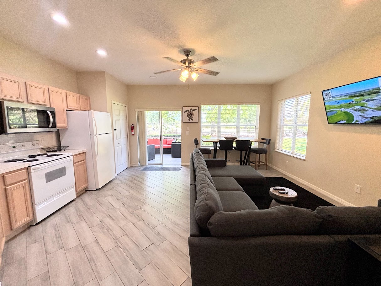 Bright open-concept kitchen and living area with wood-look flooring, comfortable seating, and easy access to the screened patio.