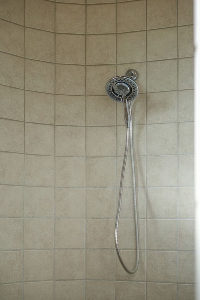Walk-in shower featuring handheld showerhead and tiled surround.