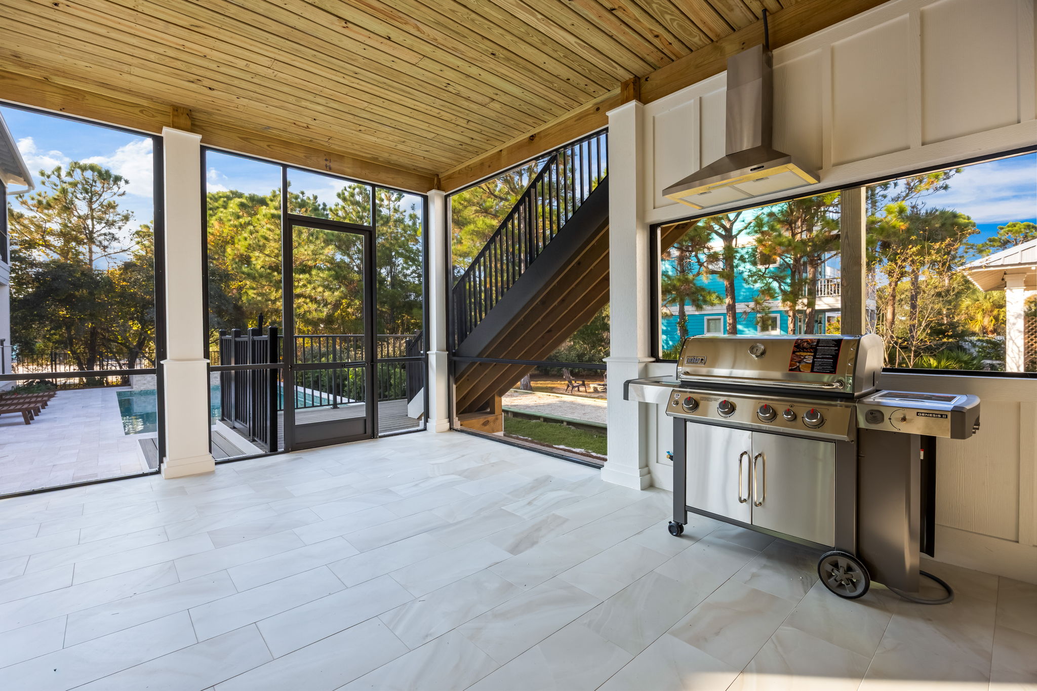 Covered outdoor kitchen and dining patio just off the main living area, featuring a gas grill with permanent propane hookup—no tanks to change or worry about—and open views toward the pool. Fully screened for comfort with wall-mounted fans, this inviting 