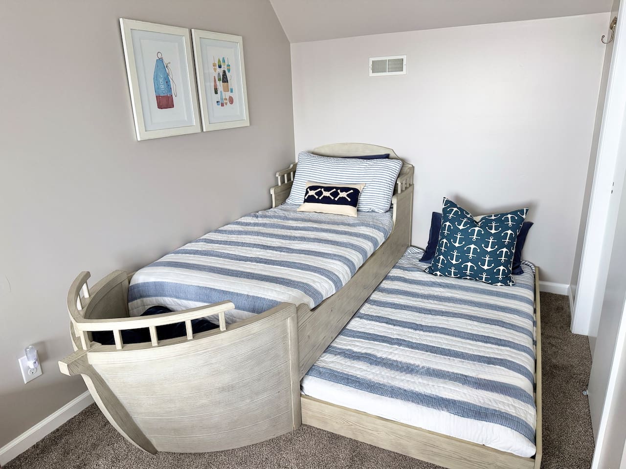 The children will love this charming kid-friendly bedroom features a unique boat-shaped bed complete with a pull-out trundle. The beds are dressed in coordinating blue and white striped quilts and accented with nautical-themed pillows.