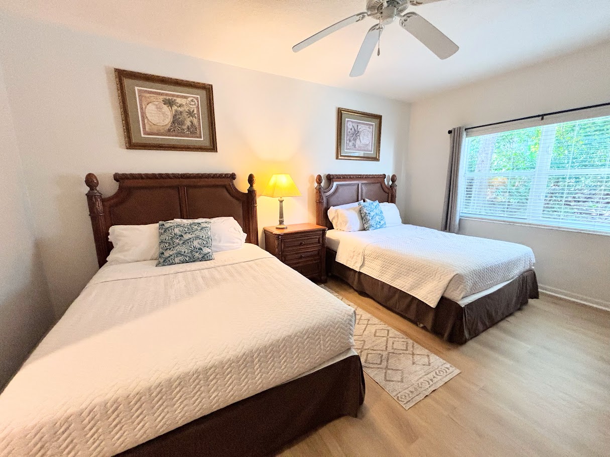 Inviting bedroom featuring two beds, wood-look flooring, ceiling fan, and a bright window view.