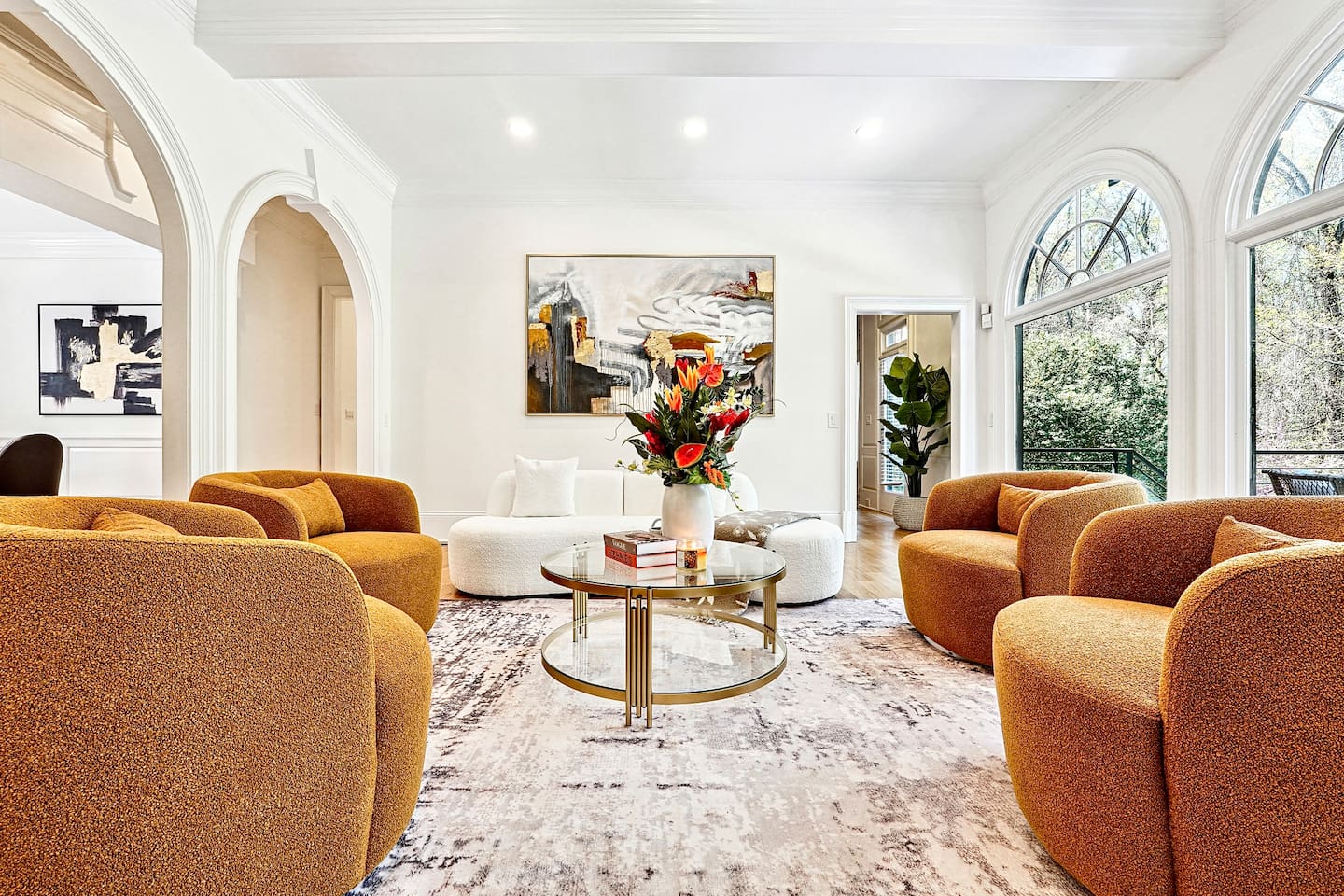 Located straight ahead from the front entry, this main-floor living room showcases a striking modern design with a round shaped contemporary sofa, four orange accent chairs, a smart TV, and a fireplace for a warm, elevated lounge experience.