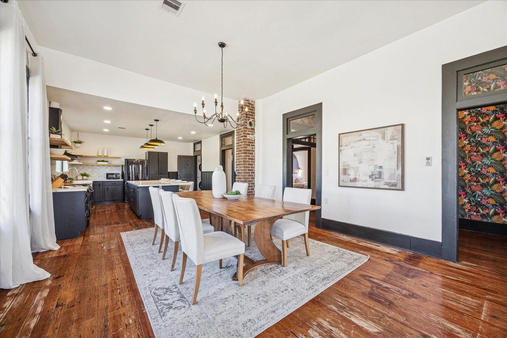 This elegant dining room blends historic charm with modern style, featuring original hardwood floors, a striking chandelier, exposed brick detail, and an open connection to both the kitchen and living areas that makes entertaining feel effortless.