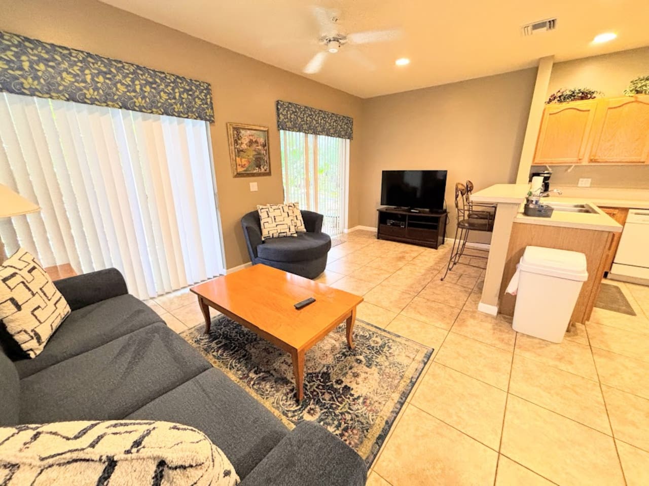Comfortable open living area with tile flooring, cozy seating, large TV, and sliding glass doors bringing in natural light.