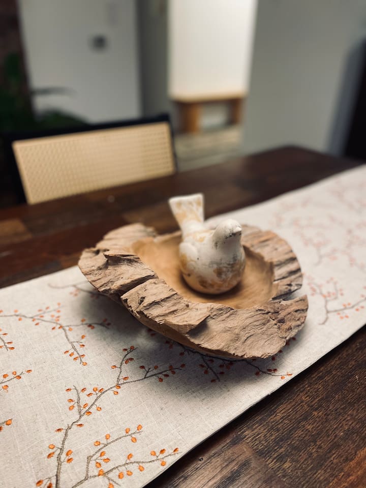 A sculptural bird rests atop a wooden burl, a naturally twisted growth in the wood, adding organic beauty and character to the table.