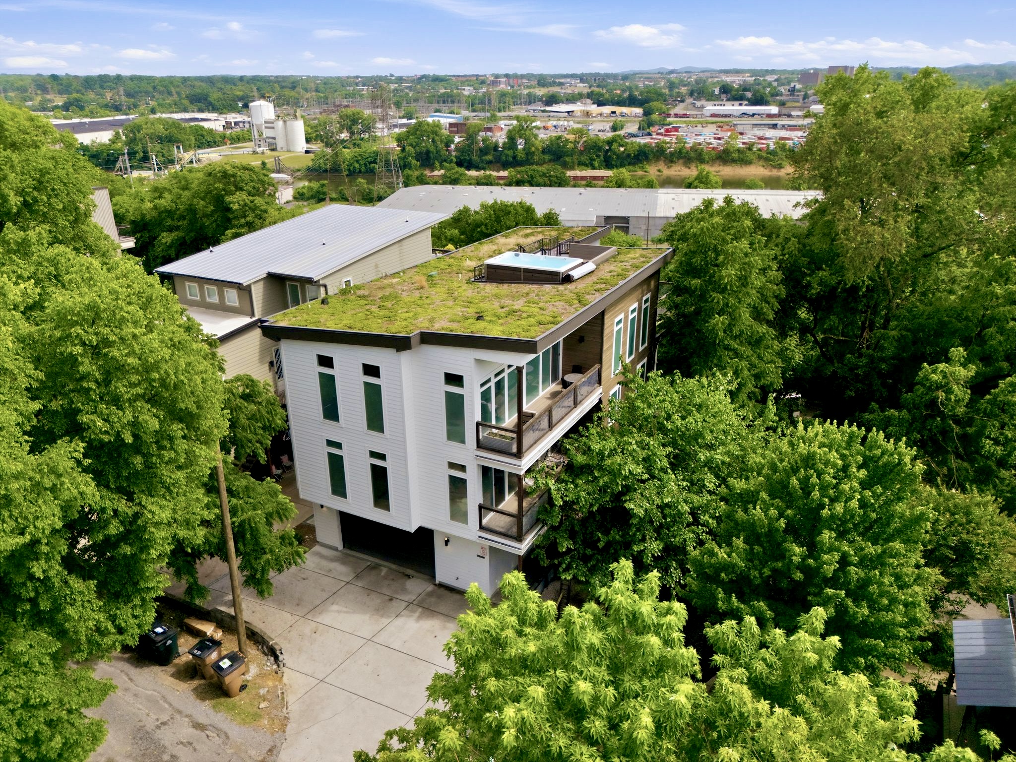 Aerial view of the full property w/ a living green roof & tree-lined surroundings.
