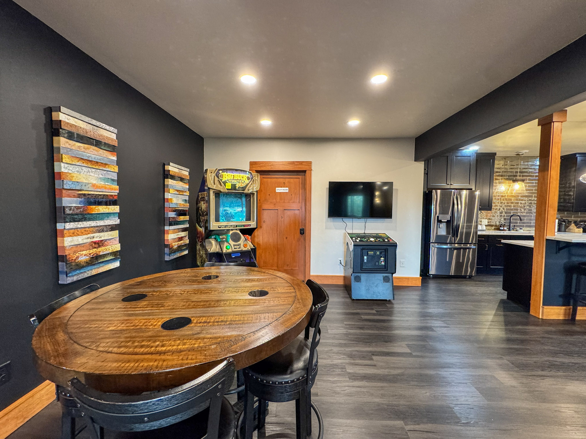 Game area with arcade machines and a gathering table beside the downstairs kitchen.