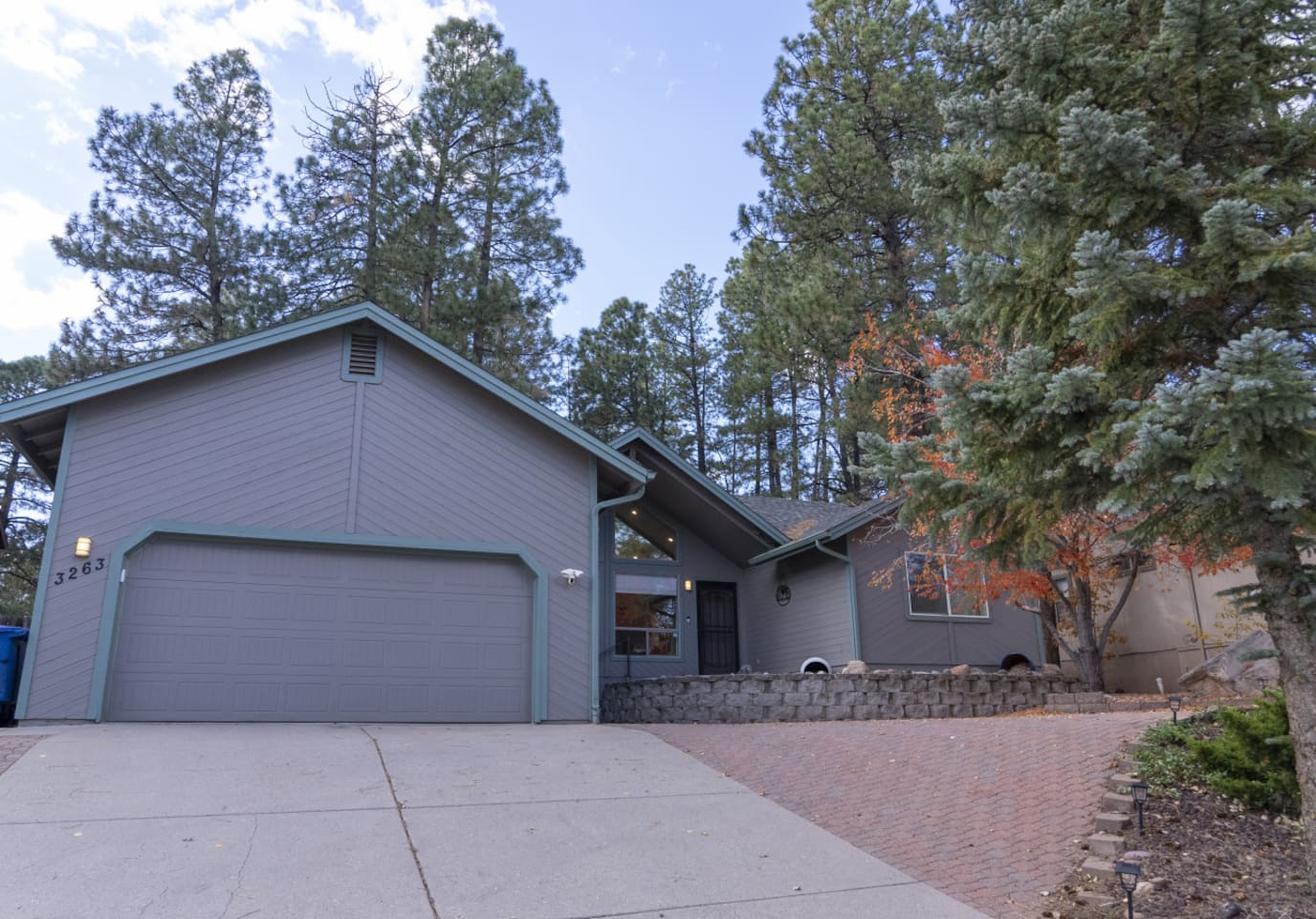 Exterior view with garage access, spacious driveway, and tall trees around the home.