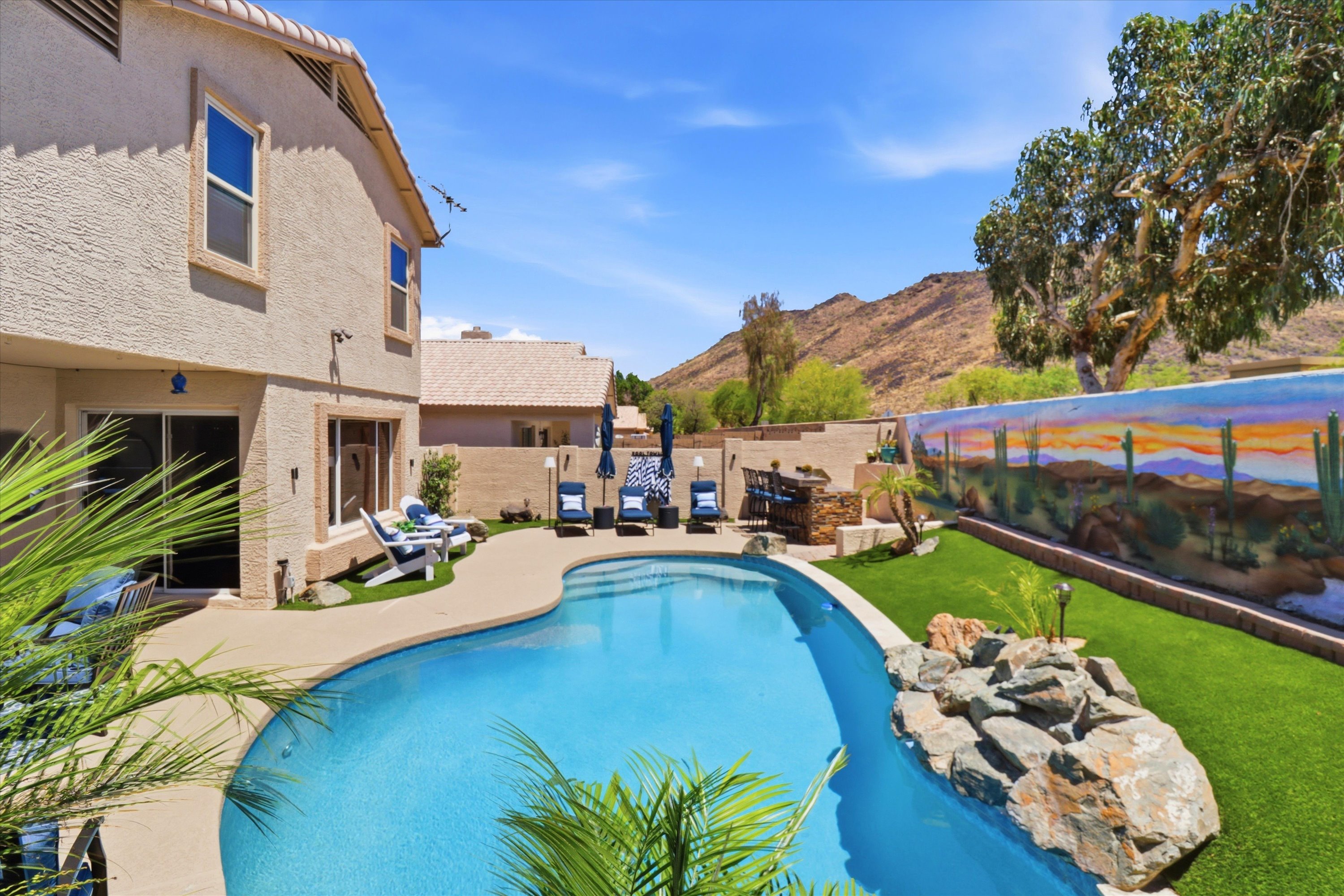 Private backyard pool with lounge seating, outdoor bar, desert mural, and mountain views for a standout outdoor retreat.