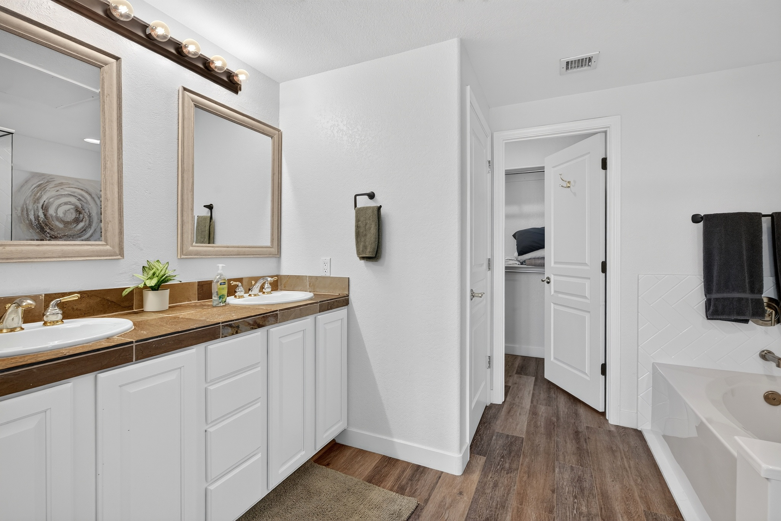 Bathroom vanity with double sinks, bright mirror lighting, cabinet storage, easy access to the nearby shower  and king bedroom 