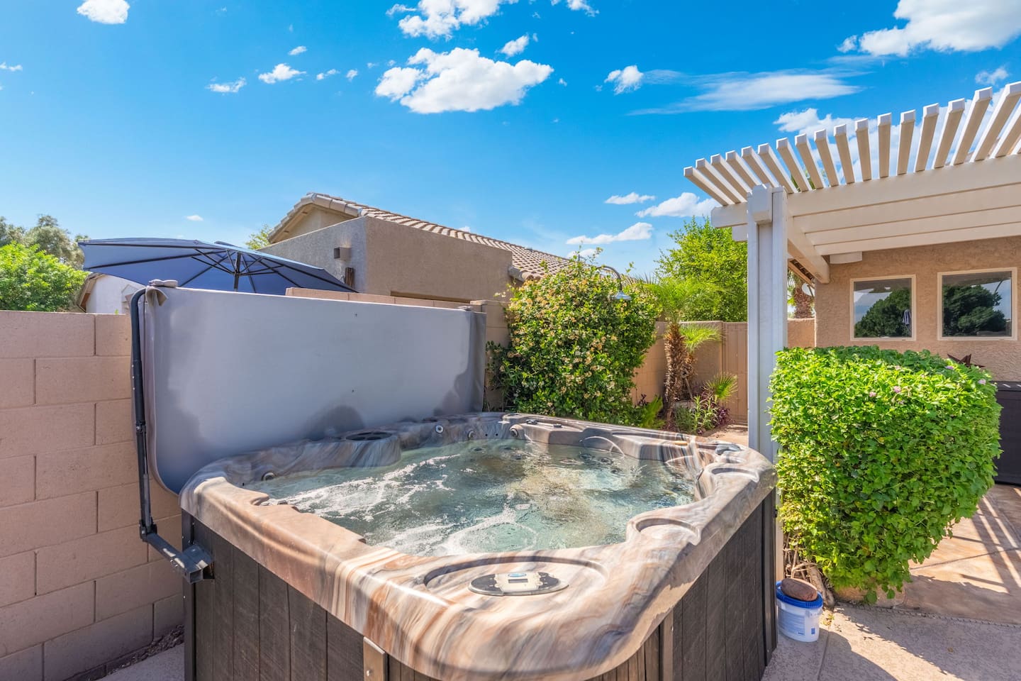 A secluded hot tub nestled in a lush, landscaped corner of the yard — the pergola overhead and greenery all around make it feel like your own private hideaway.