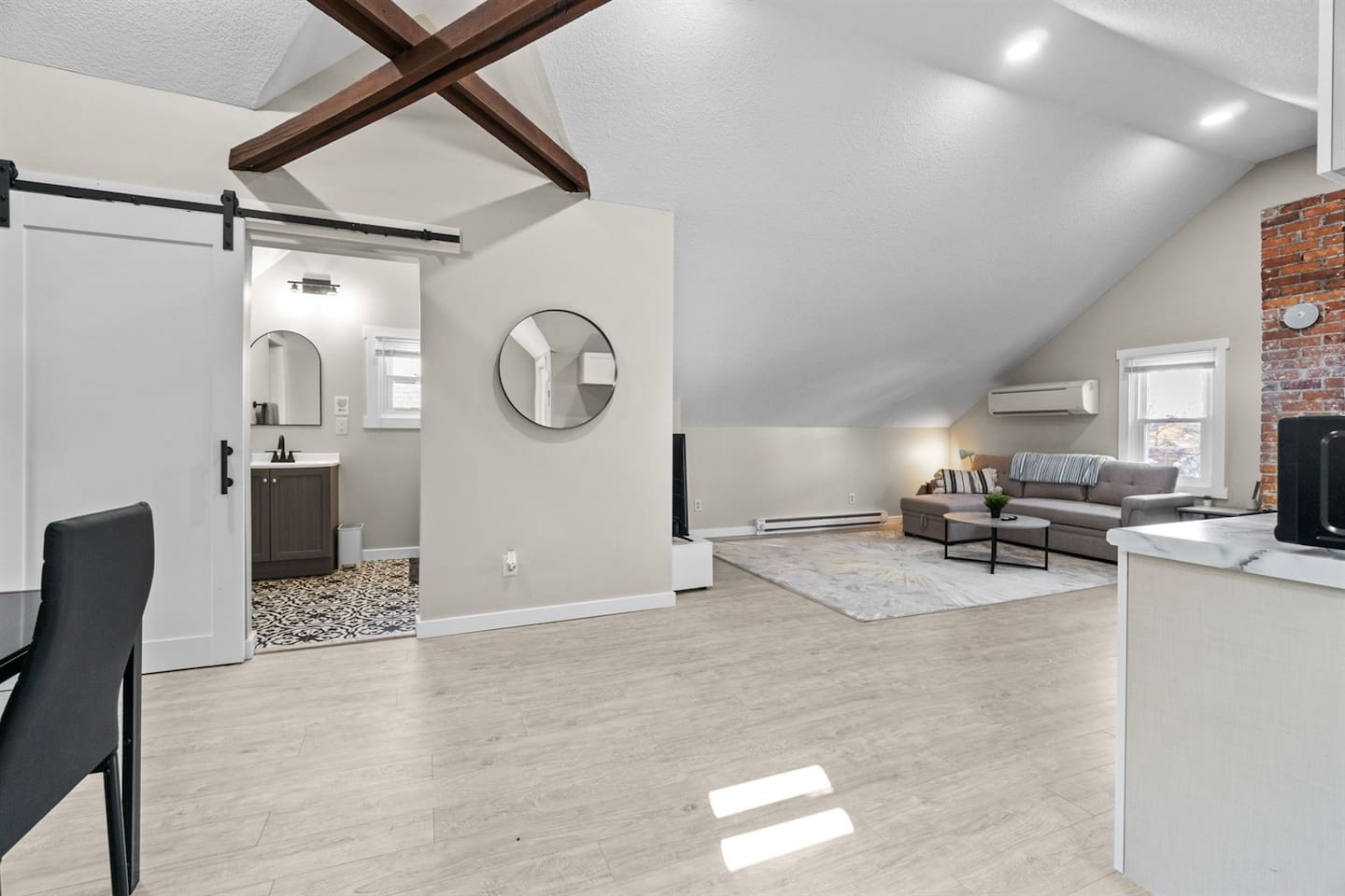 An open-concept living space filled with natural light, highlighting stunning wooden beams and charming brick accents.