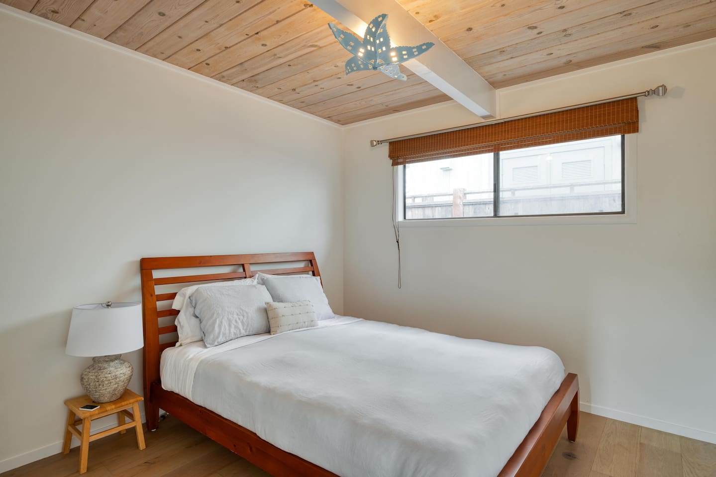 - Cozy bedroom featuring wooden bed frame with crisp white linens for rest  
- Wood paneled ceiling adds warmth and character to the inviting setting  
- Large window fills the space with daylight and neighborhood scenery  
