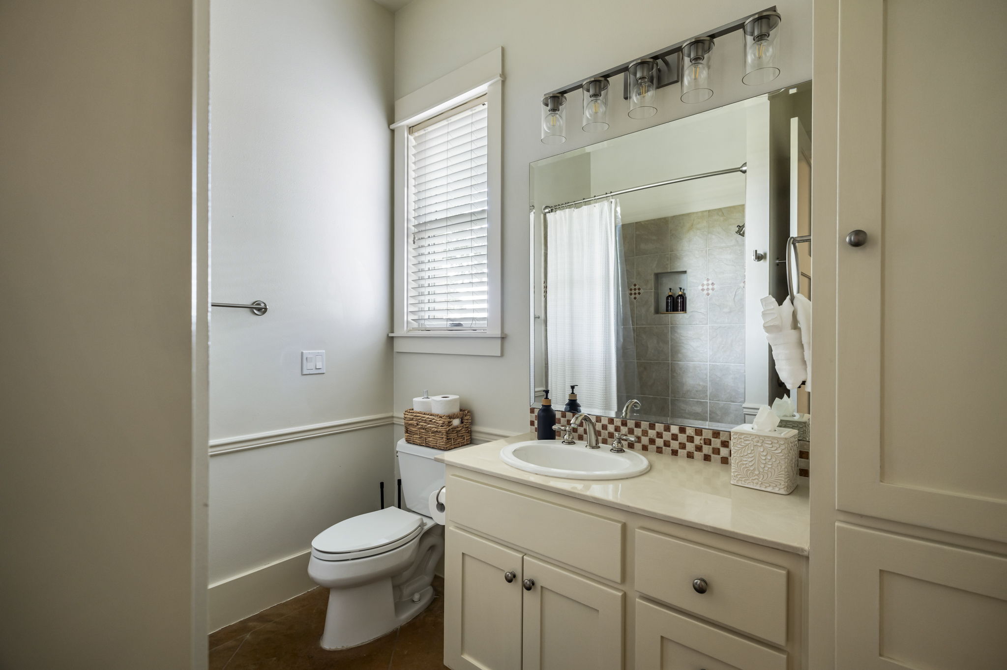 A full view of a modern bathroom featuring a clean toilet, a spacious vanity with a sink and mirror, and a tiled shower visible in the reflection